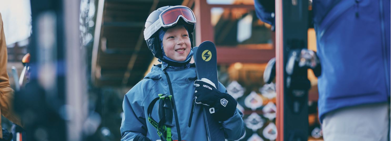 Child holds skies and smiles in his ski gear