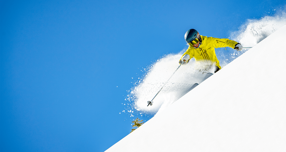 skier in yellow carves through powder on a steep hill, vibrant blue ski illuminates white snow