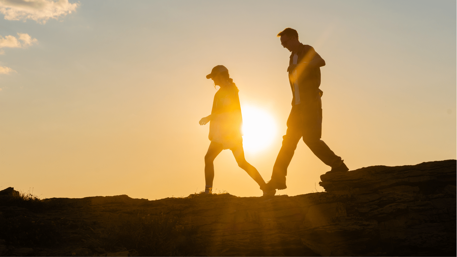 Two people hike on aspen mountain, sun setting behind them creates silhouettes