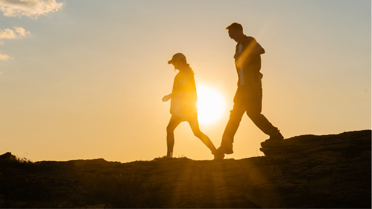Two people hike on aspen mountain, sun setting behind them creates silhouettes