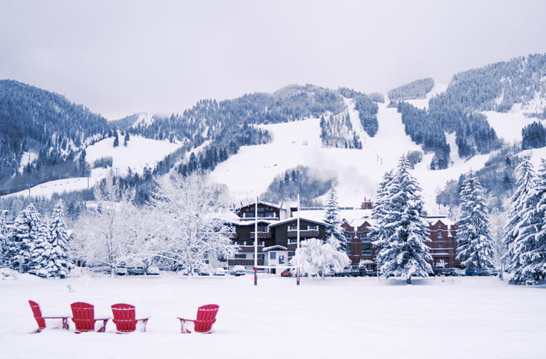 Snow and adirondack chairs in a park in Aspen with Aspen Mountain in the distance