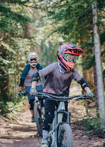 Two guests mountain bike through the family-friendly terrain of Snowmass Bike Park.