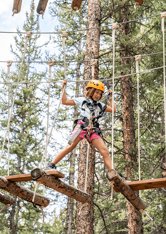 Child crosses tree bridge in the Lost Forest at Snowmass 