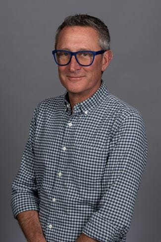 headshot of VP of sustainability at Aspen one,  Chris miller, who is a tall man who is wearing a blue and white checkered shirt with blue rimmed glasses