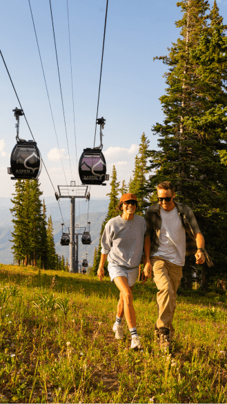 Couple walks closely as they hike under the aspen gondola at dusk