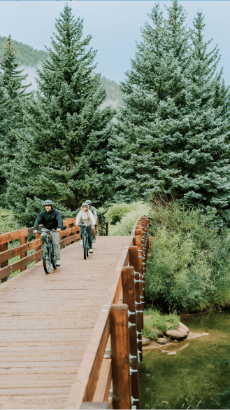 a couple rides over a wooden bridge on the aspen bike path on their ebikes
