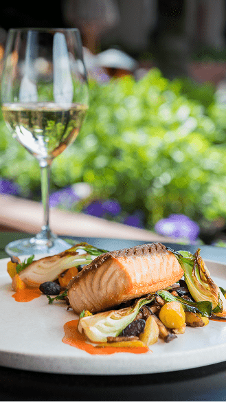 Dish at Element 47, salmon over fresh veggies, next to a glass of white wine