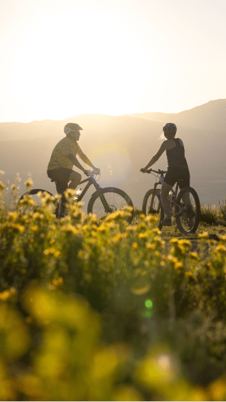 Two people look out on their bikes atop a a flower field at Aspen Snowmass