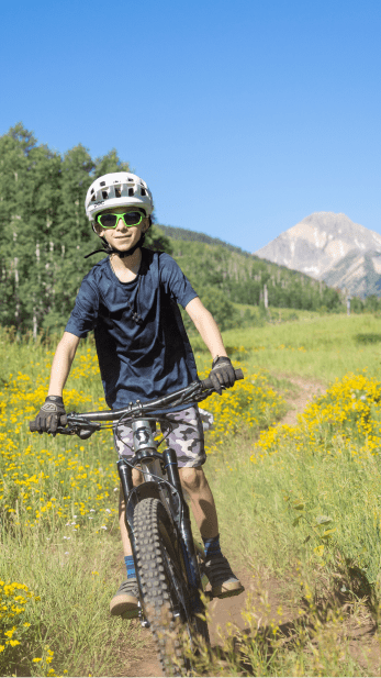 Child bikes down gental downhill trail on a sunny summer day at snowmass
