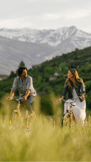 Couple biking on grassy hill on cruiser bikes in snowmass