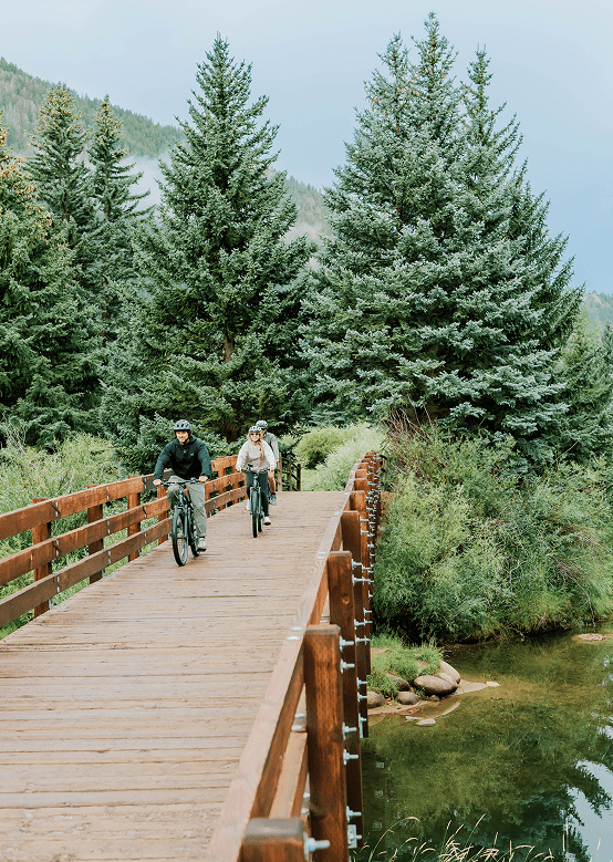 People bike over wooden bridge on bike path