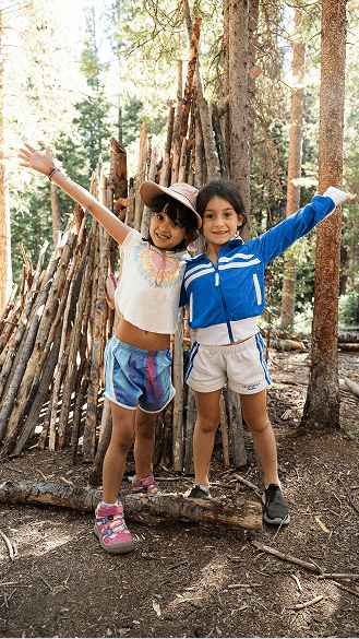 Two little girls hug each other and raise their arms up during a day camp on Snowmass Mountain
