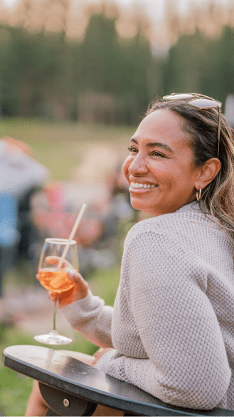 Woman holding aperol spritz smiles at the camera on snowmass mountain