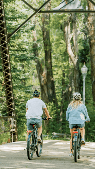 A couple rides their ebikes next to each other down the aspen bike path in the summer