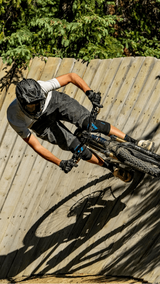 downhill biker cruises around a wooden feature at snowmass bike park