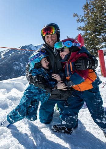 A father hugs his kids in ski clothes