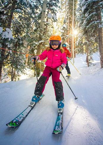 A girl learns to ski a run through the trees at Snowmass