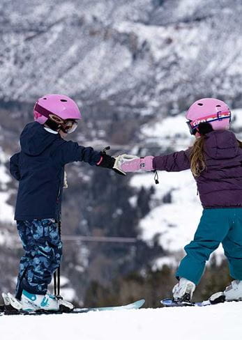 Two skiing kids fist-bump each other