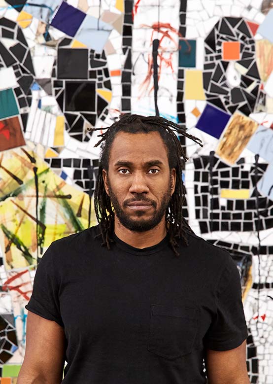 A person in black stands confidently against a colorful geometric mosaic backdrop.