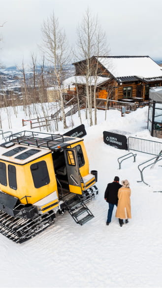Yellow snowcat with a couple standing on the snow outside a restaurant