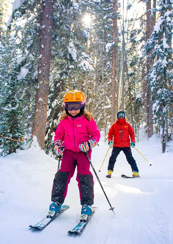 Girl skiing through the trees with her dad at Snowmass