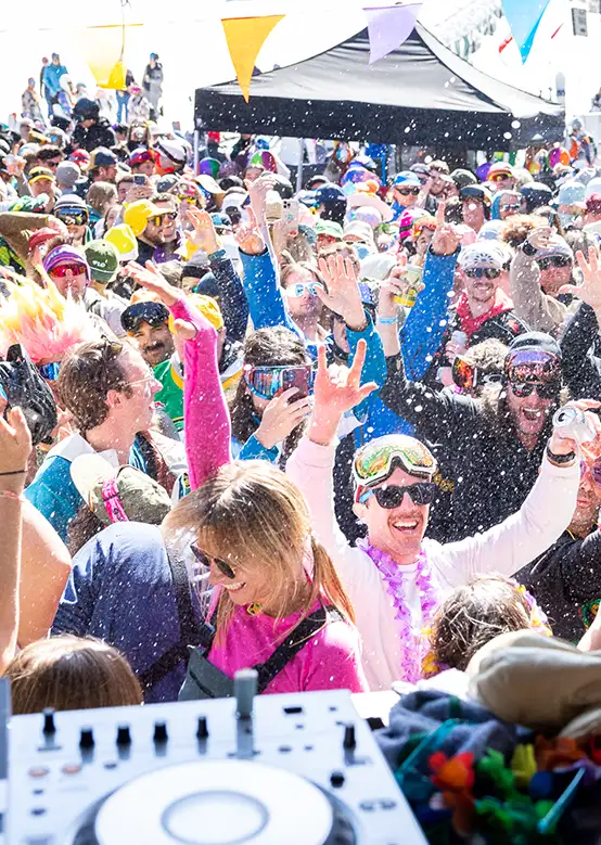A lively outdoor festival with skiers in colorful outfits dancing under banners and snowfall.