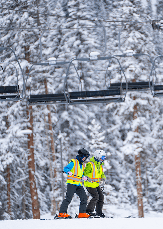 skiers in yellow vests, ski down the mountain, they are a part of the blind skier program at Aspen Snowmass