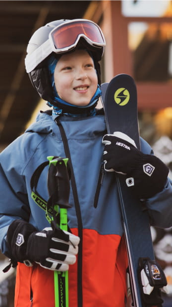 Chuld smiling with their skis and ski outfit on