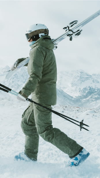 Person in green outfit carrying their skis on a ski slope
