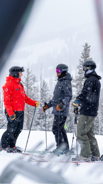 Two skiers talking to a ski pro on a mountain slope
