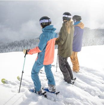 3 skiers standing in the snow on a mountain in colorful ski outfits