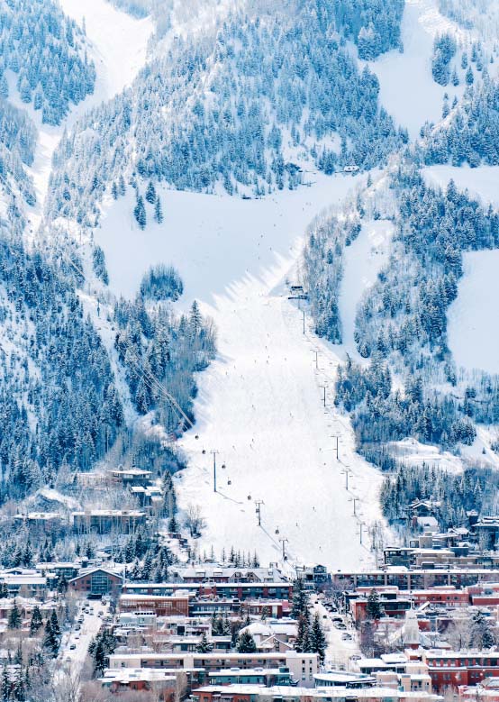 A ski lift transports skiers up a snowy slope, with an alpine town at the base and forested snow.
