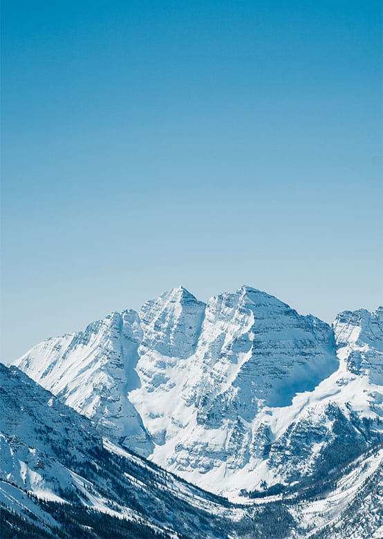 Majestic snow-covered mountain peaks rise gracefully beneath a vast, clear blue sky, creating a stunning view.
