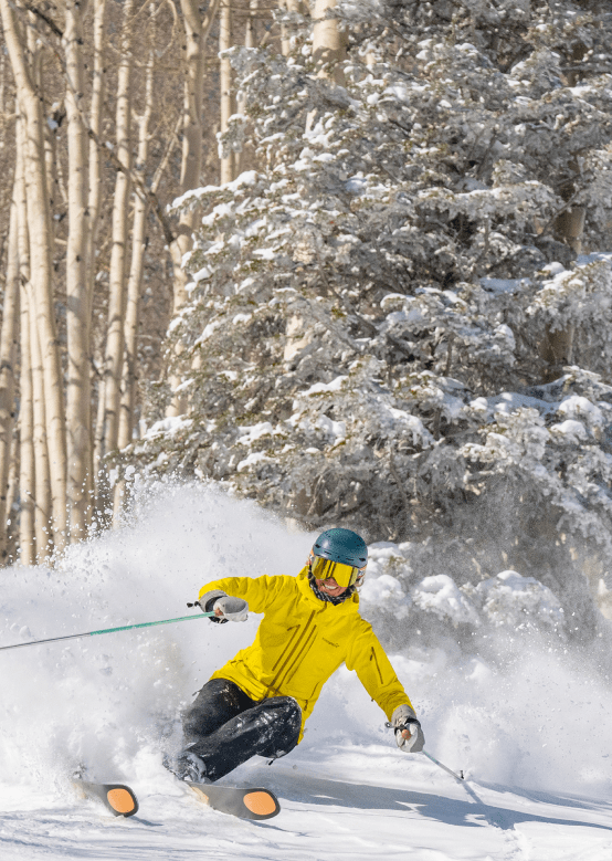 Skier in yellow jacket skiing through powder in the trees at Aspen Snowmass