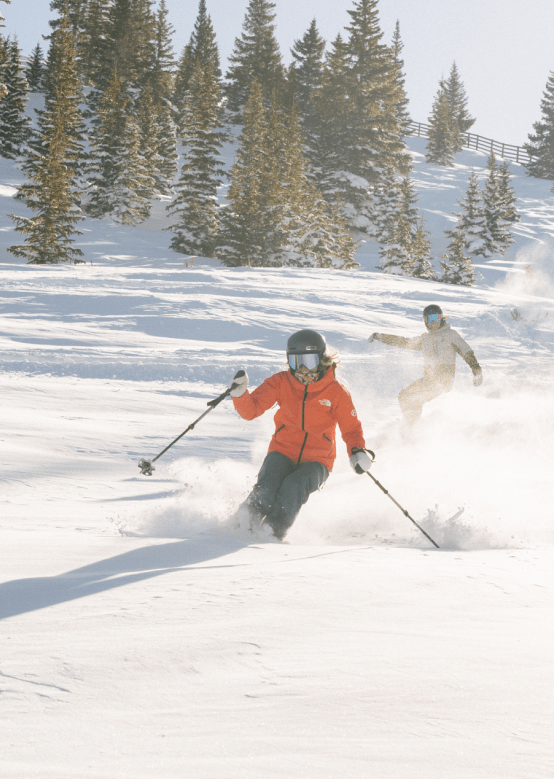 Skier and snowboarder cutting through powder at Aspen Snowmass ski resort