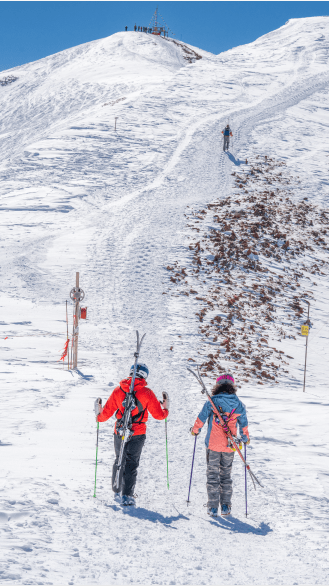 Ski instructor and their client pack skies on their back and start up the rocky incline of the Aspen Highlands Bowl