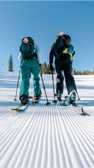 two people frombehind, as they uphill up untouched groomer runs on a bluebird day
