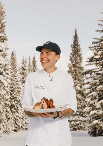 Headshot of Emily Oyer, standing in the snow holding a plate of chicken