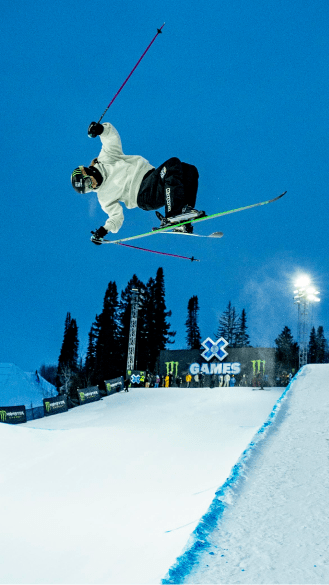 Dark blue dusk sky over the xgames half pipe, skier is airborne over the pipe