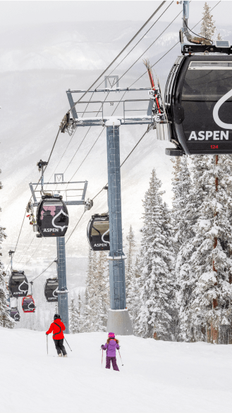 Ski instructor and child ski on aspen mountain under the aspen gondola