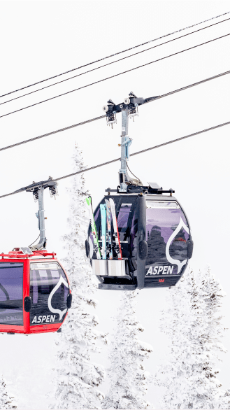 two gondolas pass eachother on the cables, on a snowy day, carrying skies on the outside of the car at aspen snowmass