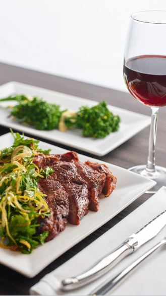 steak on a white plate, green salad on top, red glass of wine at Aspen Snowmass