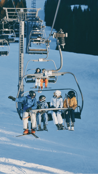 a family of four on a chairlift on aspen snowmass, chairs behind the family are still in the shade of early morning runs