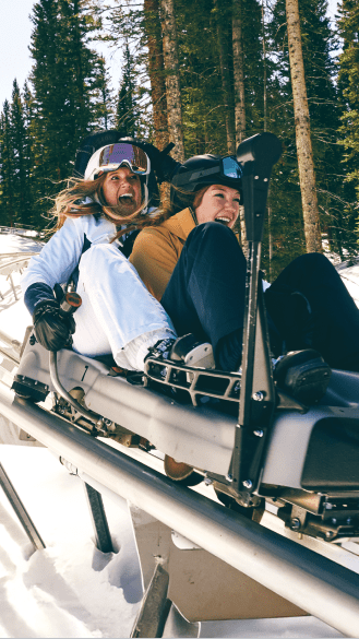 Two women scream in excitement as they take the alpine coaster in their ski gear