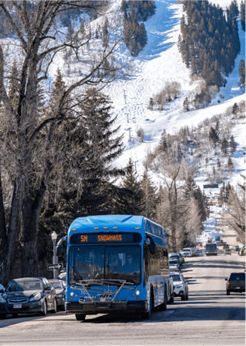 Blue RFTA bus drives down main street, Aspen mountain ski resort can be seen in background