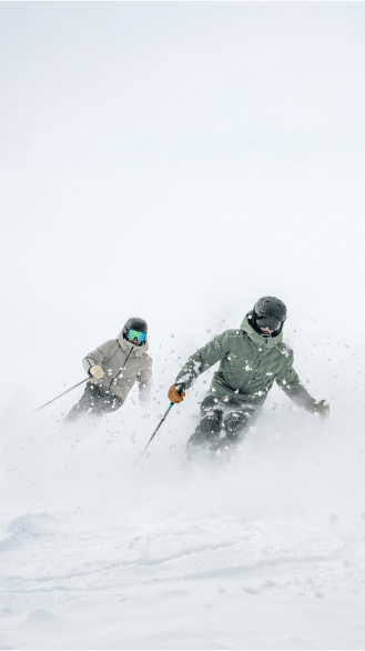 two people ski through knee deep powder in their aspen collection ski pants and jacket