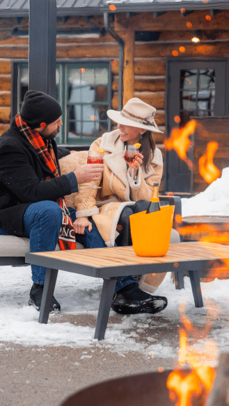 Couple laughes and cheers their Aperol Spritz at the Cabin, by a roaring fireplace at Snowmass
