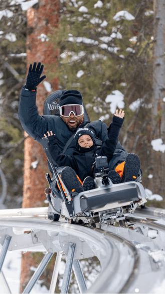 father and son raise their hands above their head and cheer as they go around a turn on the alpine coaster