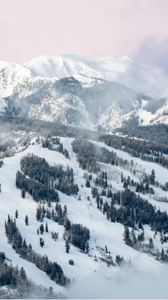 Pink skies over white ski runs at Buttermilk, green trees offset the snowy mountain