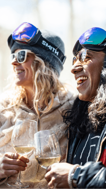 two people cheers their wine glasses together, dressed up for gay ski week